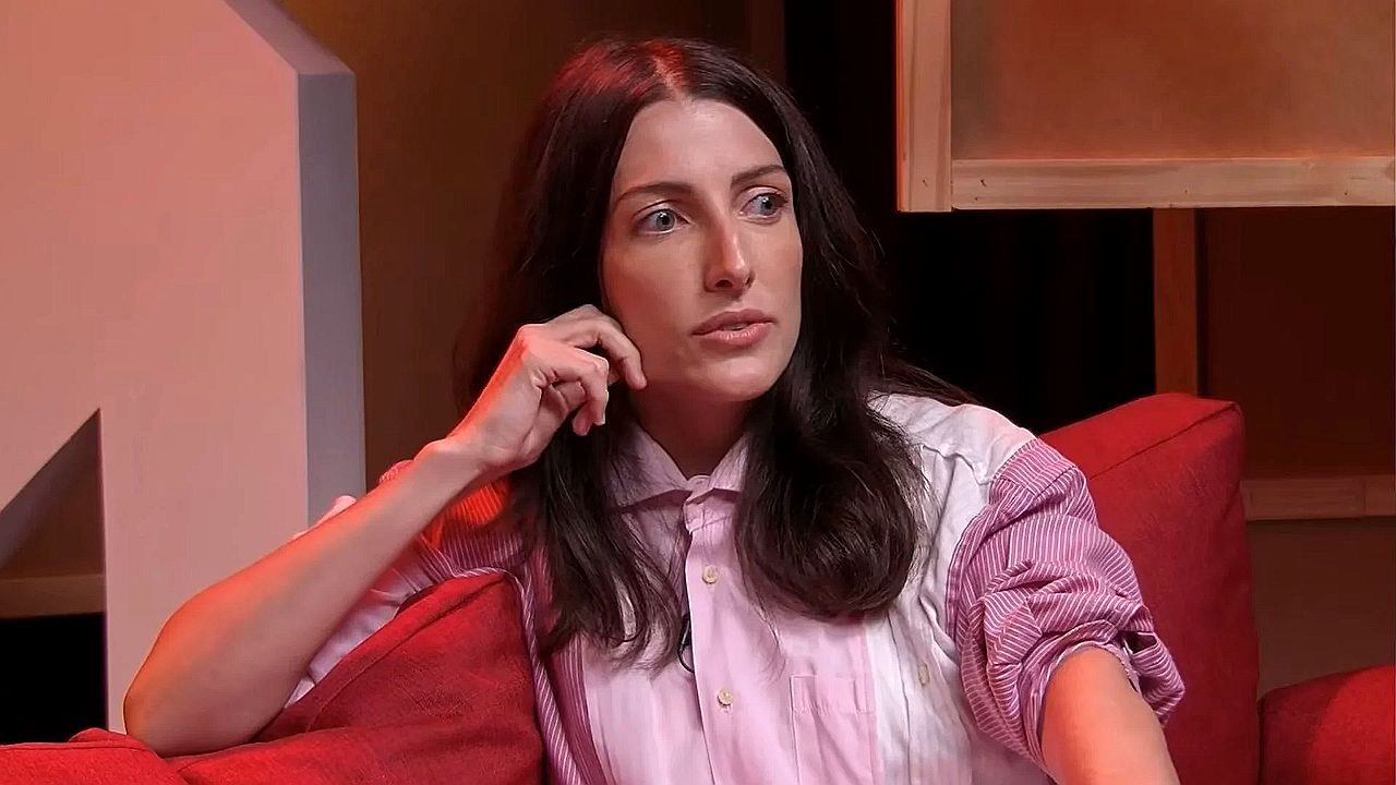 Mulher de camisa listrada participa de entrevista em programa com iluminação vermelha no estúdio