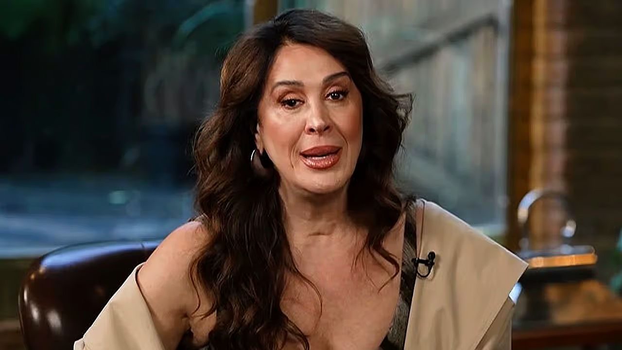 Texto Alternativo disse: Atriz de cabelos longos fala durante entrevista sentada em estúdio com microfone preso à roupa