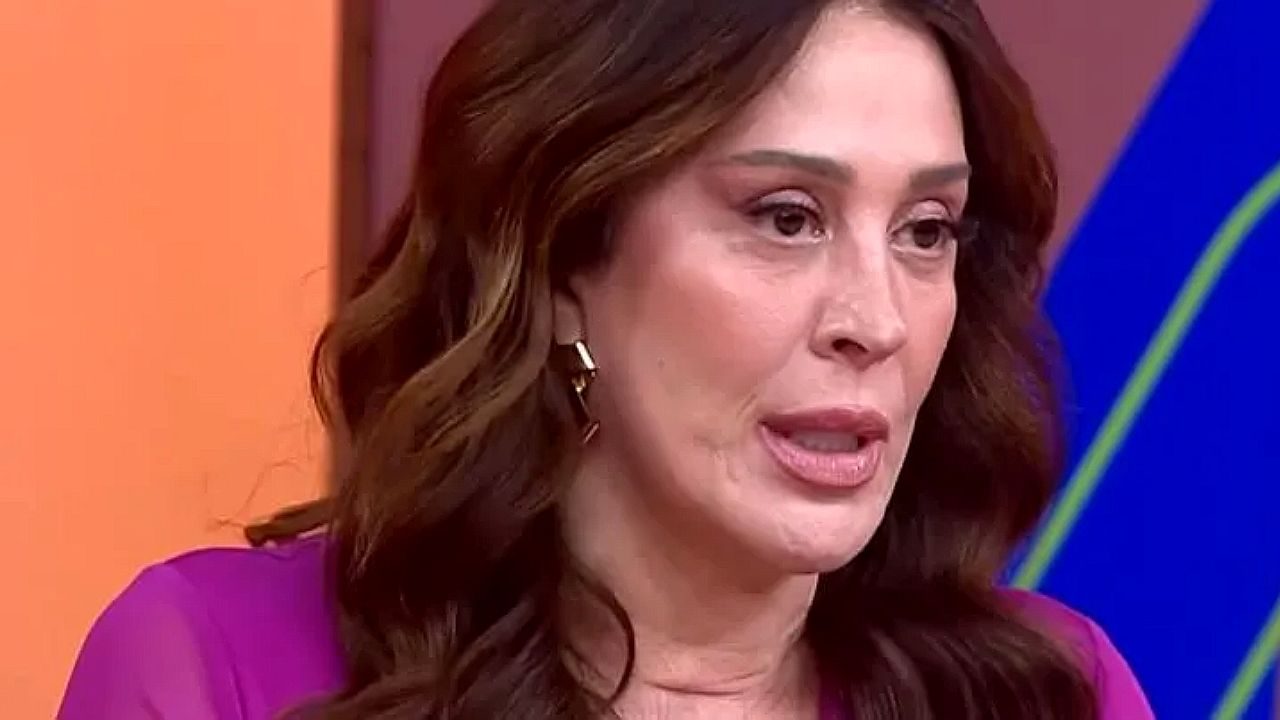 Mulher fala com expressão séria durante participação em programa de TV em estúdio colorido