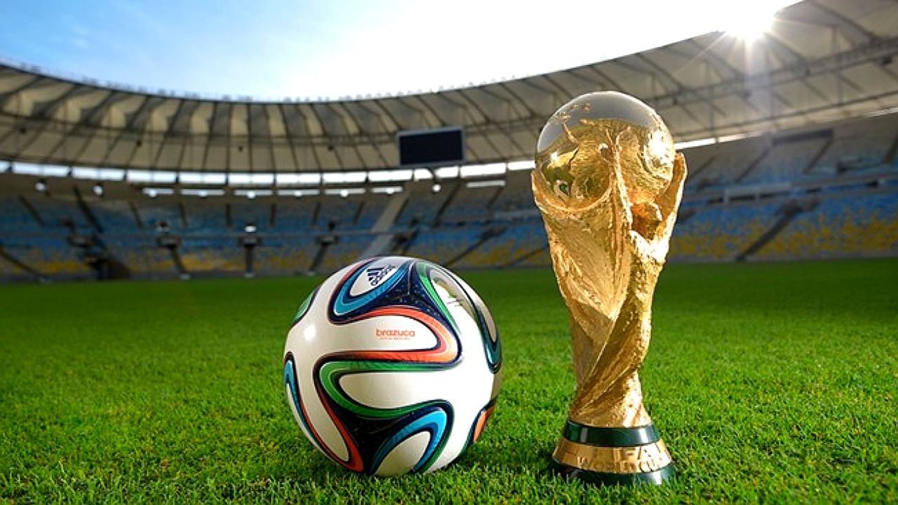 Troféu da Copa do Mundo e bola oficial sobre o gramado de estádio antes de partida do torneio