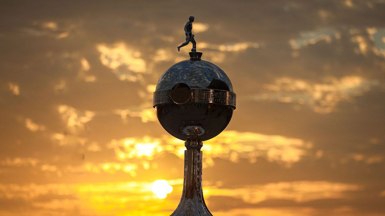 Taça da Conmebol Libertadores em destaque com o céu alaranjado e o sol se pondo ao fundo em imagem promocional do torneio de futebol