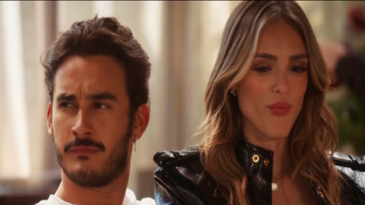 Homem de barba olha desconfiado ao lado de mulher de cabelo longo e jaqueta preta em cena de novela