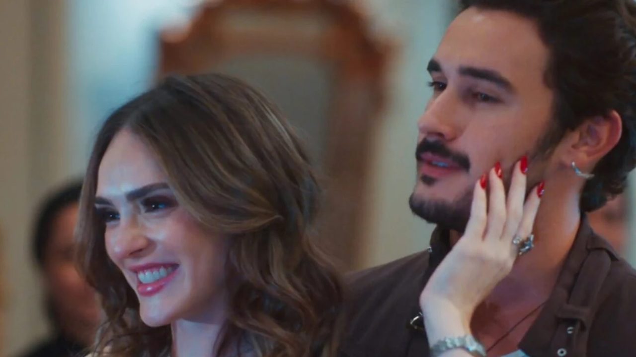 Mulher sorri enquanto toca o rosto de homem com barba em cena romântica de novela