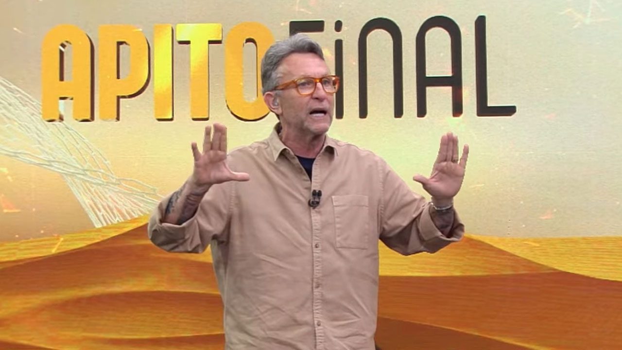 Craque Neto gesticulando em frente ao telão com logo do programa Apito Final