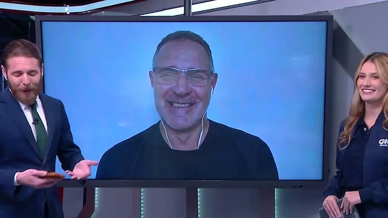 Apresentadores da CNN Brasil ao lado de telão com entrevistado participando por videochamada ao vivo no estúdio