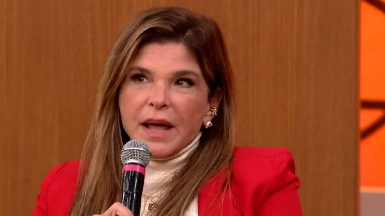 Cristiana Oliveira fala ao microfone usando blazer vermelho durante participação em programa de televisão