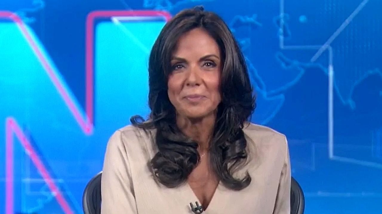 Cristina Ranzolin durante apresentação de telejornal da RBS TV em estúdio com telão de notícias ao fundo