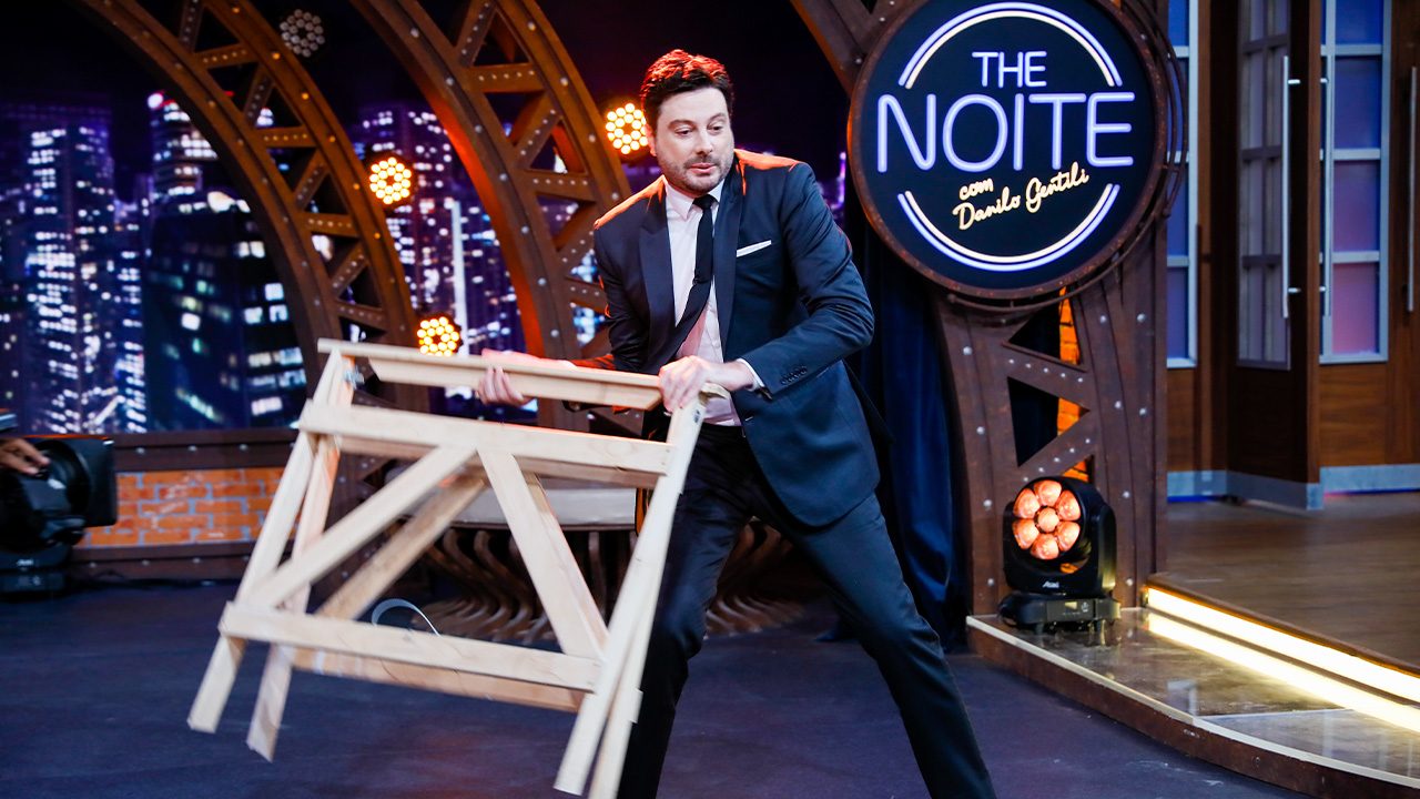 Danilo Gentili segura estrutura de madeira no palco do The Noite durante gravação do talk show no SBT