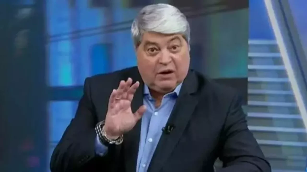 O apresentador José Luiz Datena aparece em cena do programa Tá na Hora, exibido pelo SBT. Vestindo paletó escuro e camisa azul clara, ele gesticula com a mão levantada em sinal de ênfase, enquanto se dirige à câmera com expressão séria. A imagem transmite o tom direto e enérgico característico de suas apresentações jornalísticas.