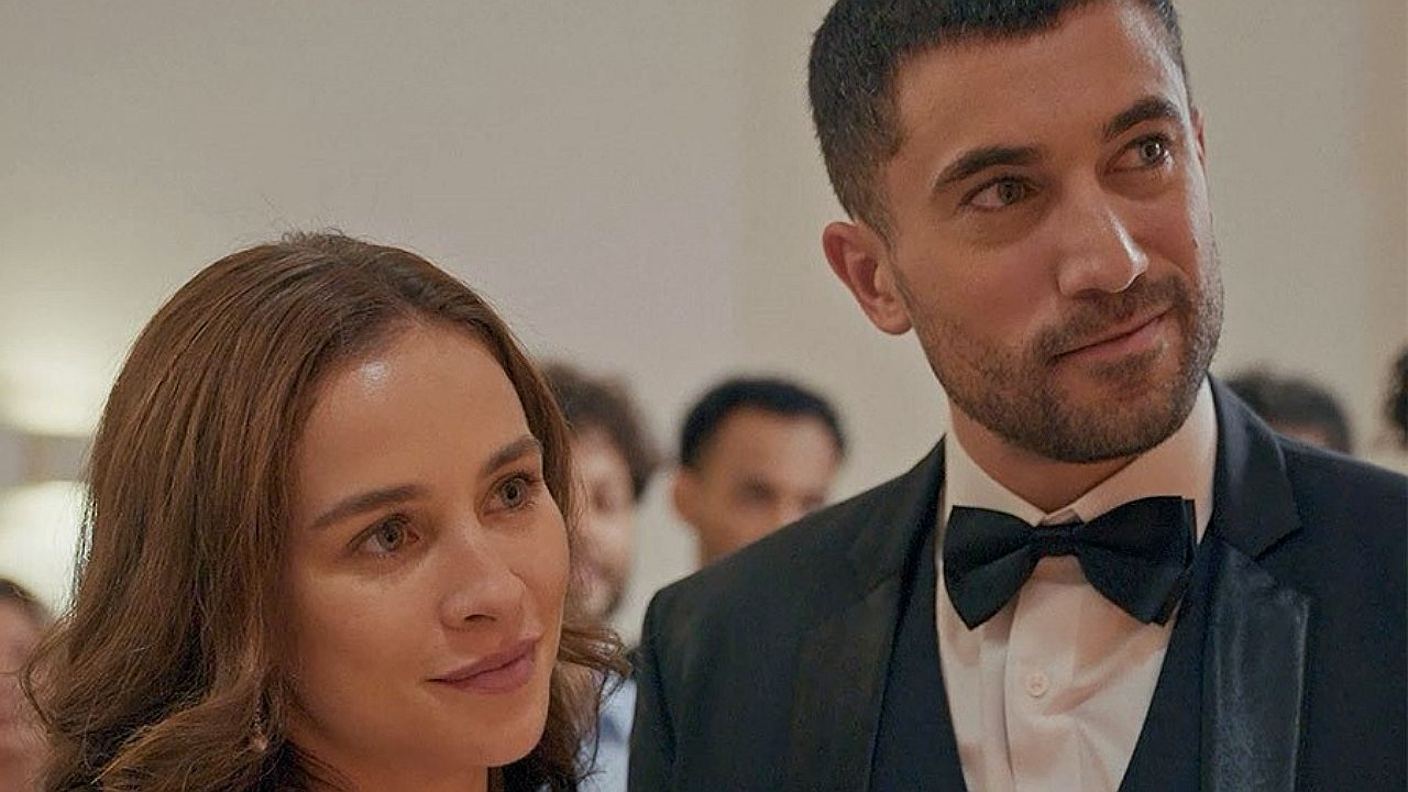 Casal elegante em evento formal observa algo com expressão atenta em cena de festa