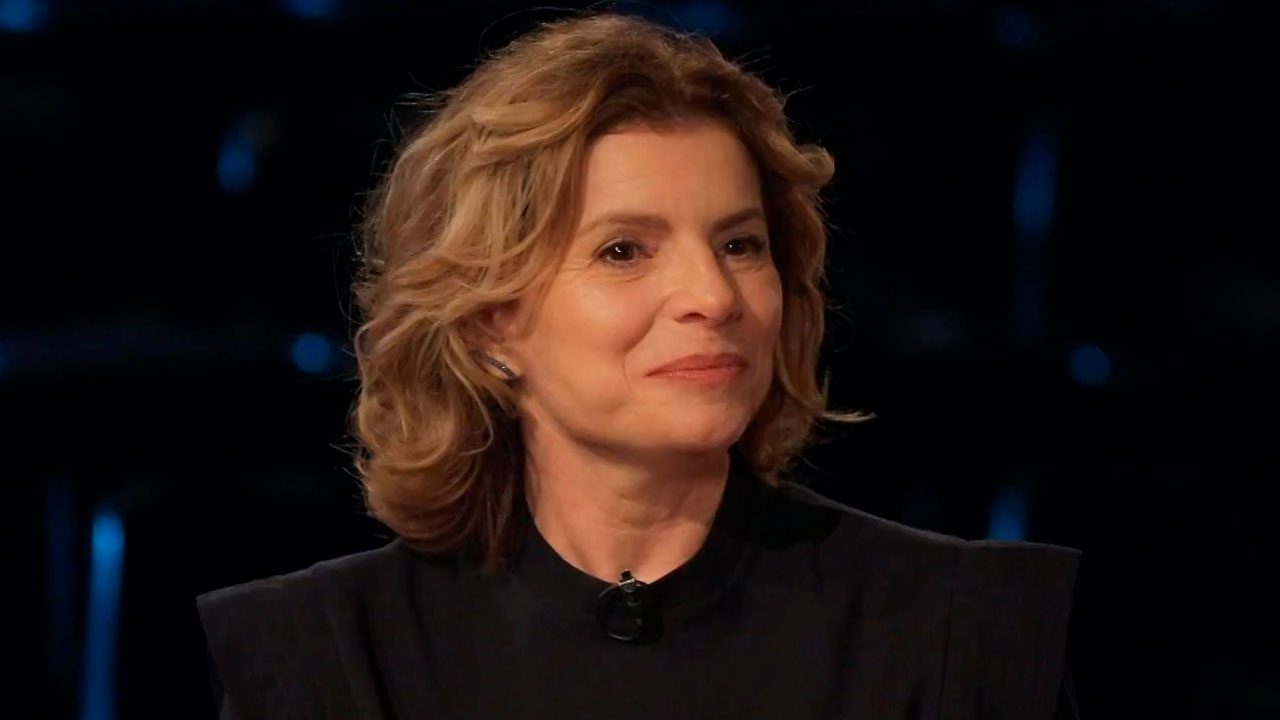 Débora Bloch sorrindo durante participação entrevista ao Fantástico com fundo escuro e iluminação pontual