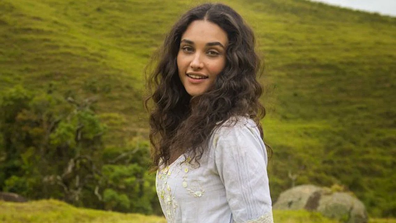 Débora Nascimento sorri em cenário rural durante cena da novela Êta Mundo Bom!