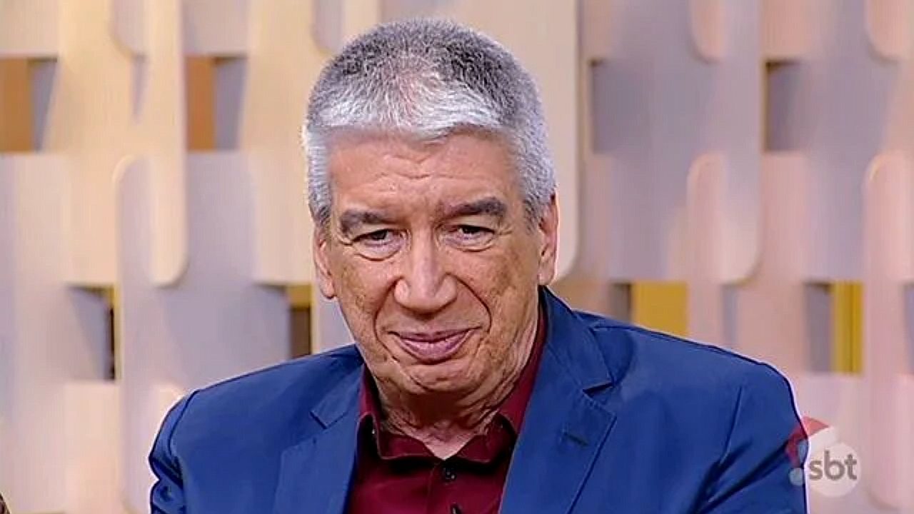 Apresentador de cabelo grisalho usa blazer azul durante programa do SBT no estúdio da emissora