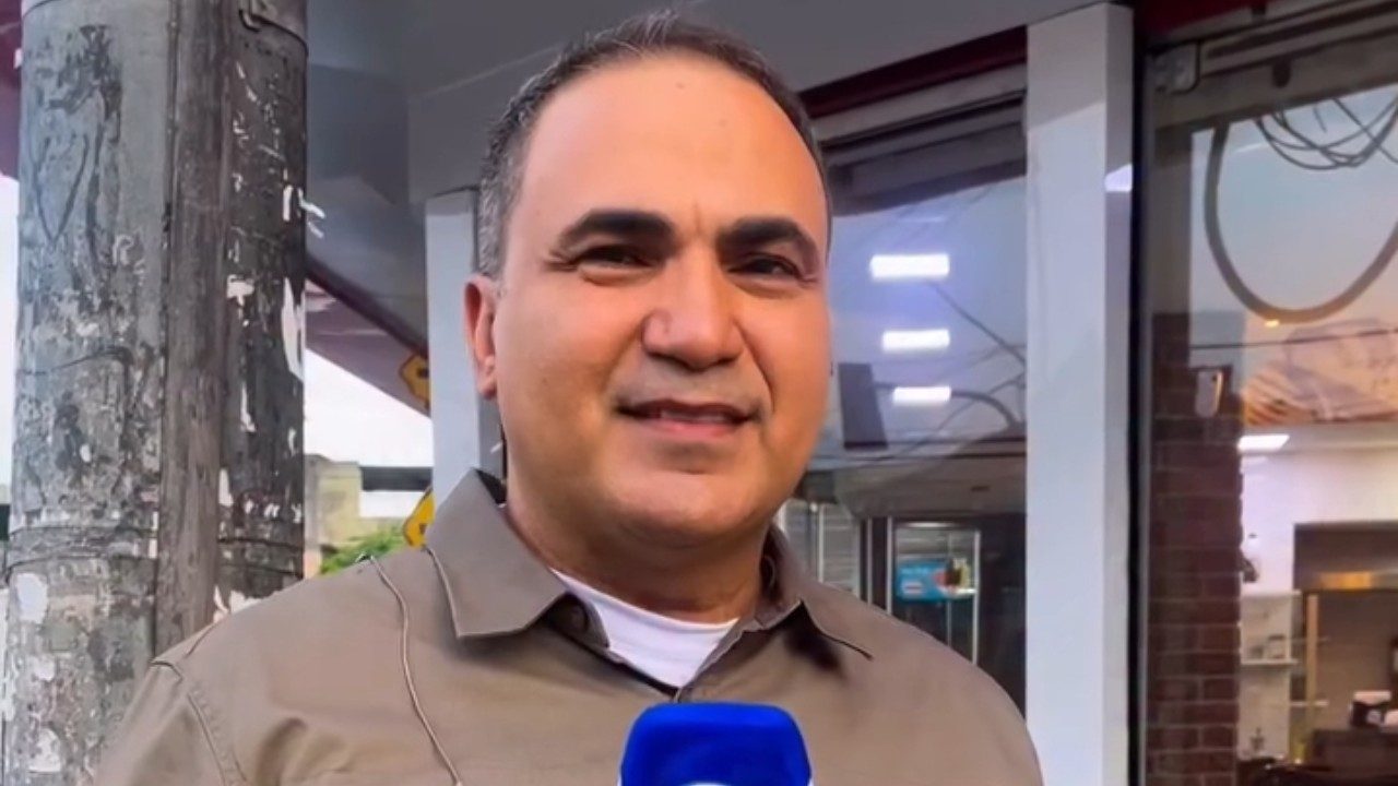 Dennes Queiroz com microfone da Record durante reportagem em frente a estabelecimento comercial na rua