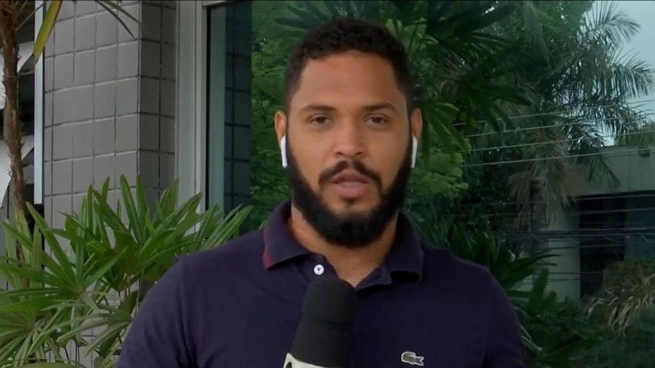 Homem com fone de ouvido segura microfone durante entrada ao vivo em reportagem externa com plantas ao fundo