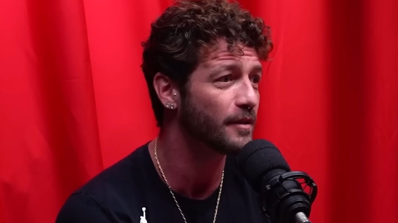 Diogo Venturieri, de cabelos encaracolados e barba, fala em um microfone com fundo vermelho em participação em podcast