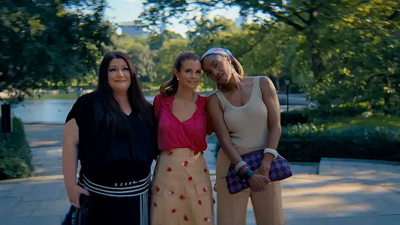 Três mulheres posam juntas em parque arborizado durante passeio ao ar livre em cena de série de comédia dramática