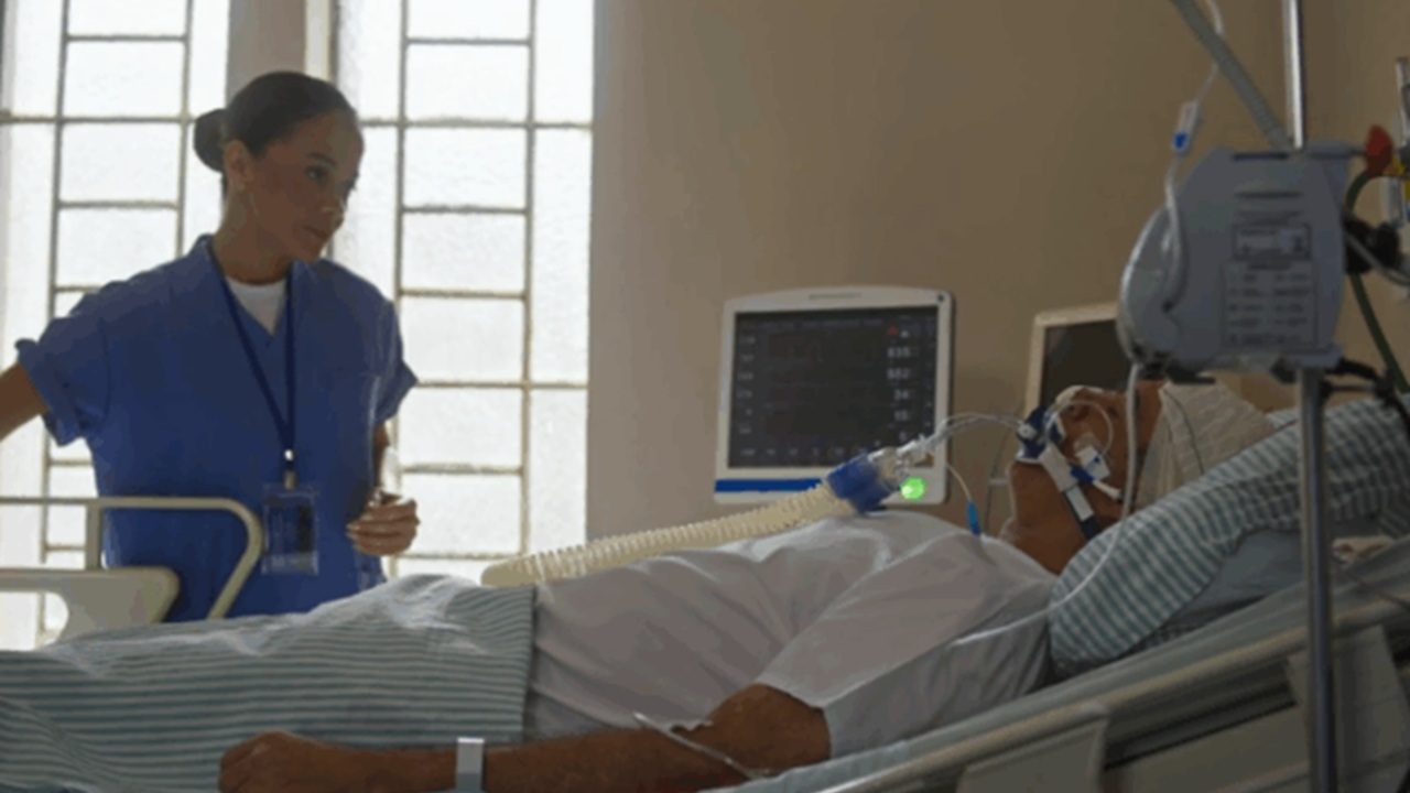 Cena da novela Dona de Mim mostra uma profissional de saúde ao lado de um paciente entubado em um leito de hospital, cercado por equipamentos médicos e monitor cardíaco
