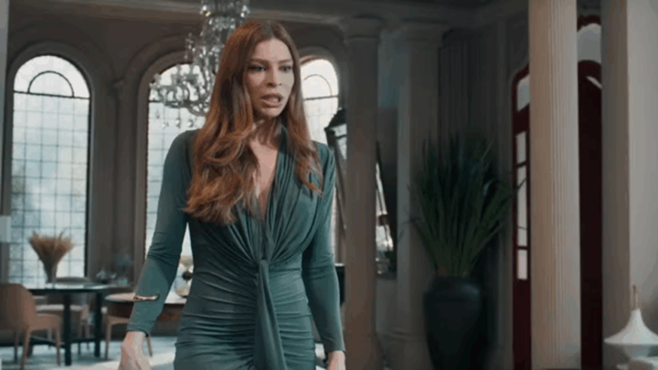 Mulher de vestido verde caminha com expressão preocupada em sala elegante em cena da novela Três Graças