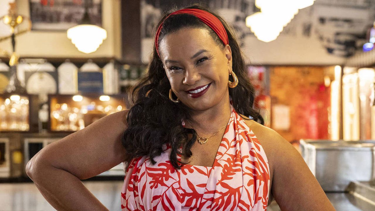 Solange Couto caracterizada como Dona Jura sorrindo em cenário de bar em cena da novela Dona de Mim