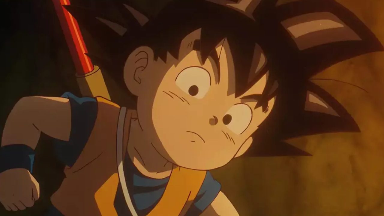 Personagem de anime com cabelos pretos arrepiados e expressão determinada aparece iluminado por luz amarelada, vestindo roupa laranja e azul e carregando bastão nas costas em cena de Dragon Ball