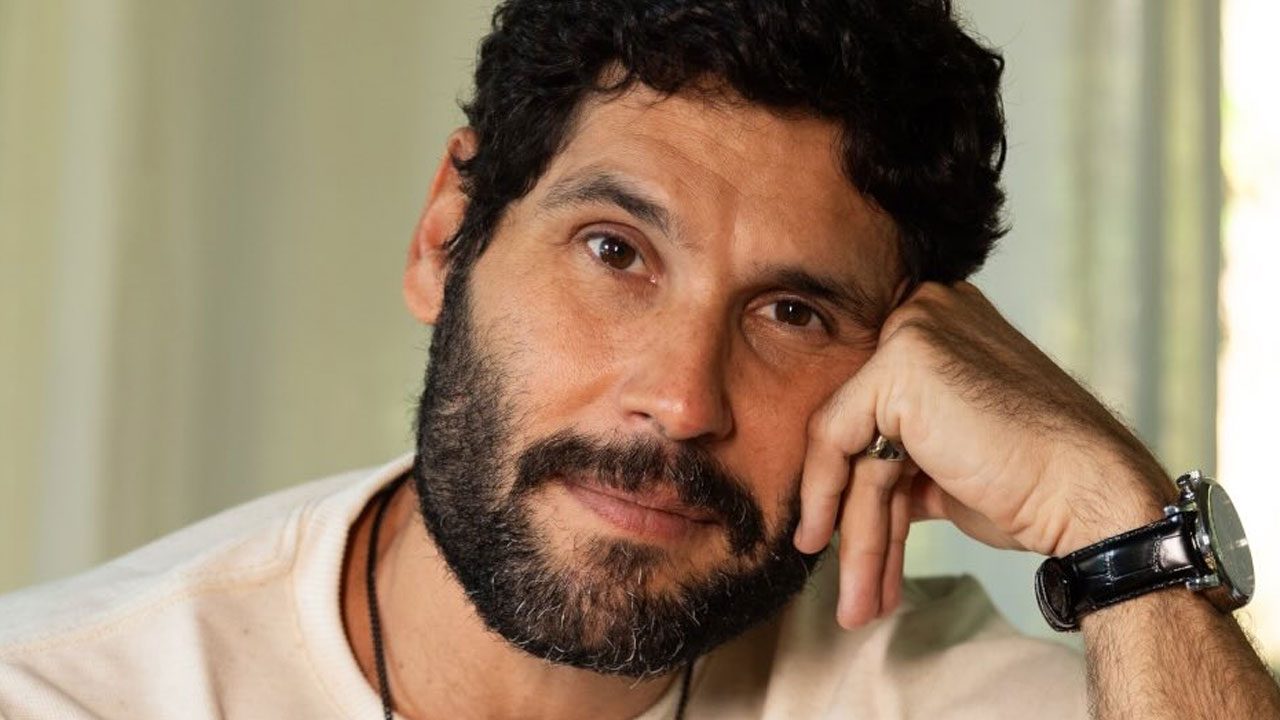 Dudu Azevedo com expressão serena apoia o rosto na mão em ambiente interno iluminado