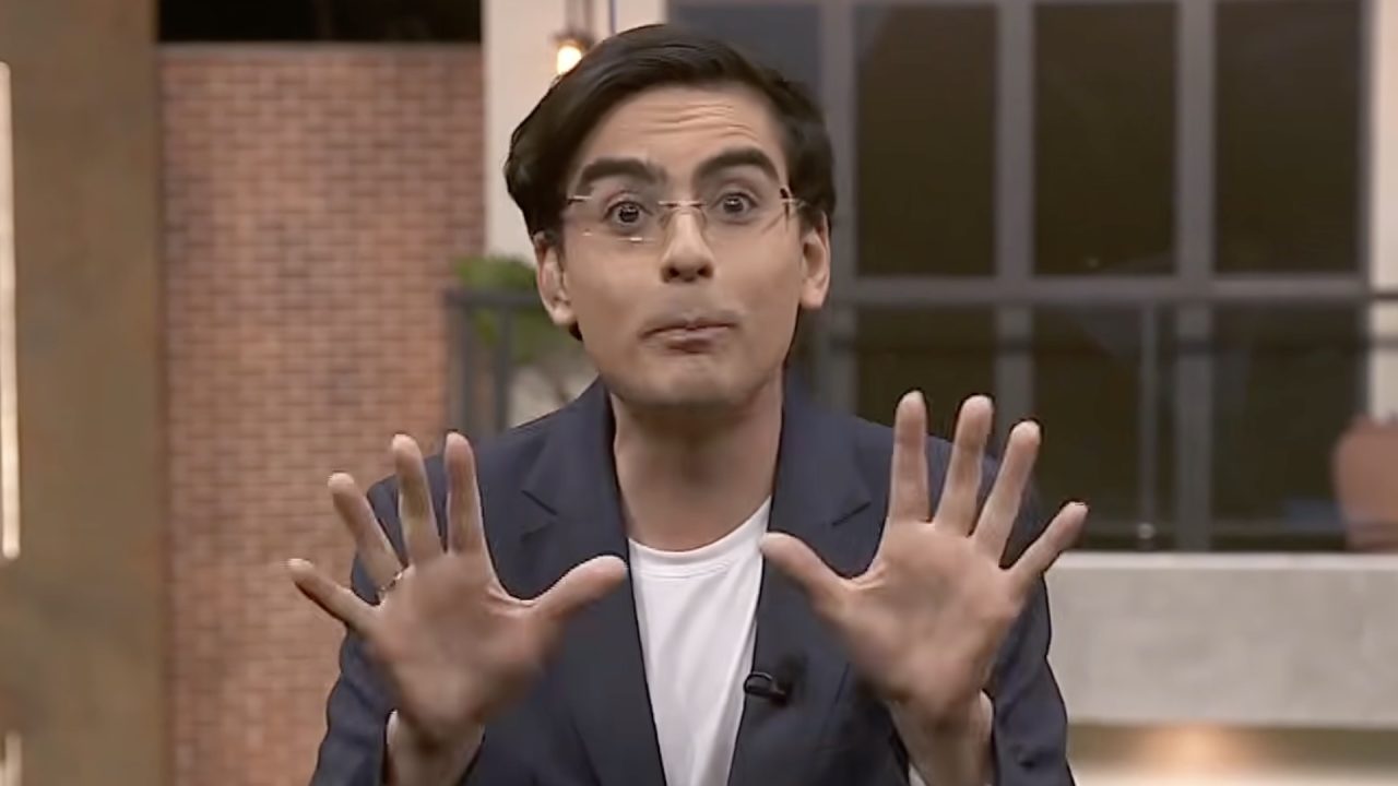 Dudu Camargo, de blazer cinza e camiseta branca, gesticula com mãos erguidas no estúdio da Casa do Patrão