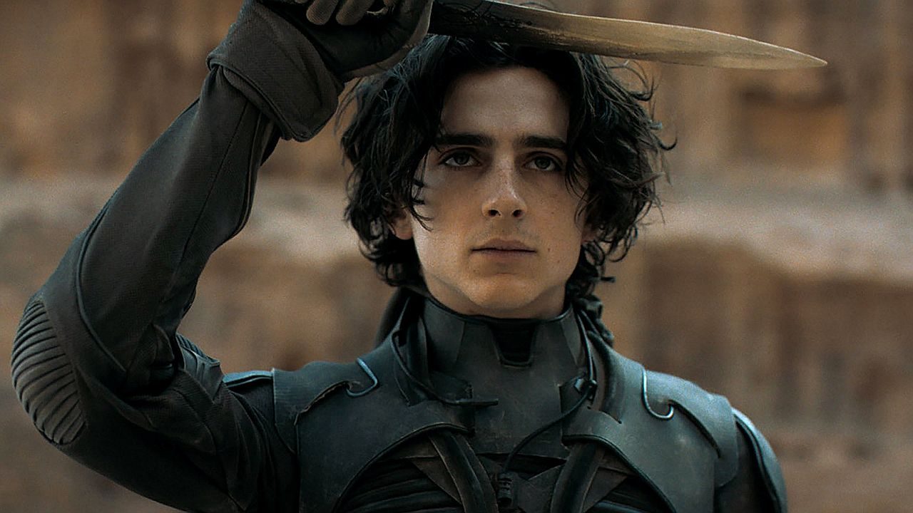 Paul Atreides ergue faca em cena do filme Duna com traje de combate e expressão determinada