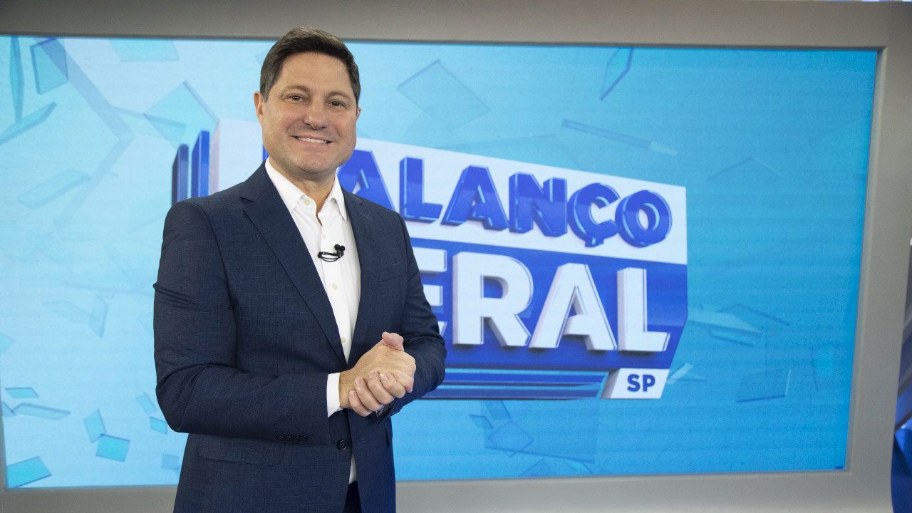 Eleandro Passaia sorrindo em frente ao telão do Balanço Geral SP durante apresentação no estúdio da Record