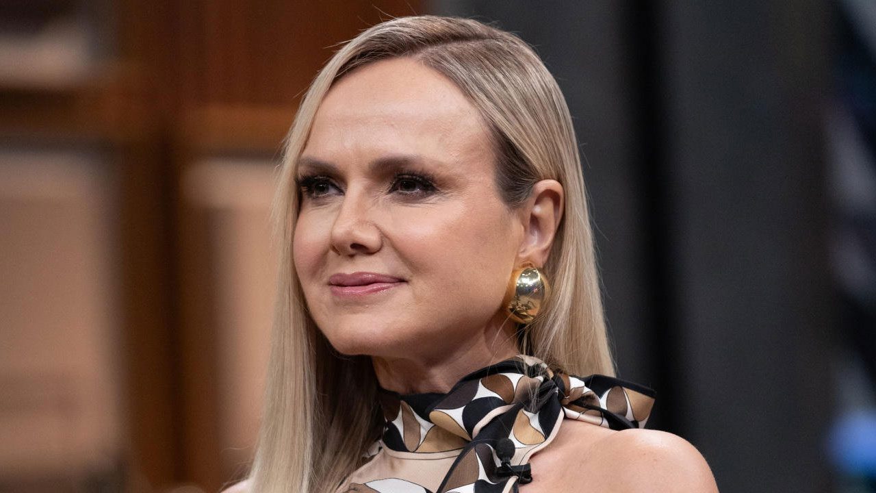 Apresentadora Eliana com cabelo loiro liso, usando um lenço com estampa geométrica e brinco grande dourado