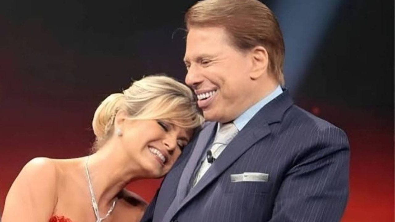Eliana e Silvio Santos sorrindo juntos em um estúdio de TV, demonstrando carinho e amizade — ela encostada no ombro dele, ambos bem-humorados e elegantes
