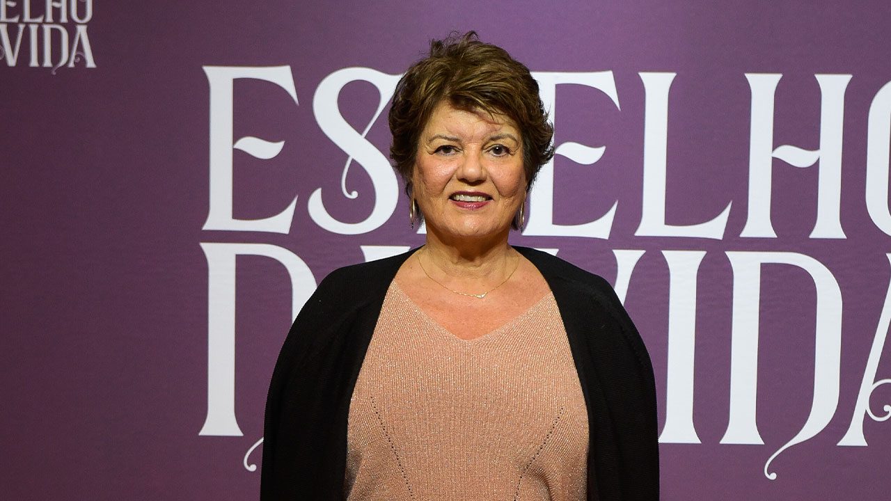 Elizabeth Jhin sorrindo em frente ao painel da novela Espelho da Vida durante evento de divulgação