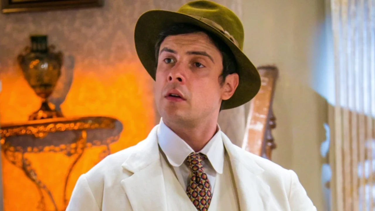 Candinho com expressão surpresa usando terno claro e chapéu em cena da novela Êta Mundo Bom da Globo