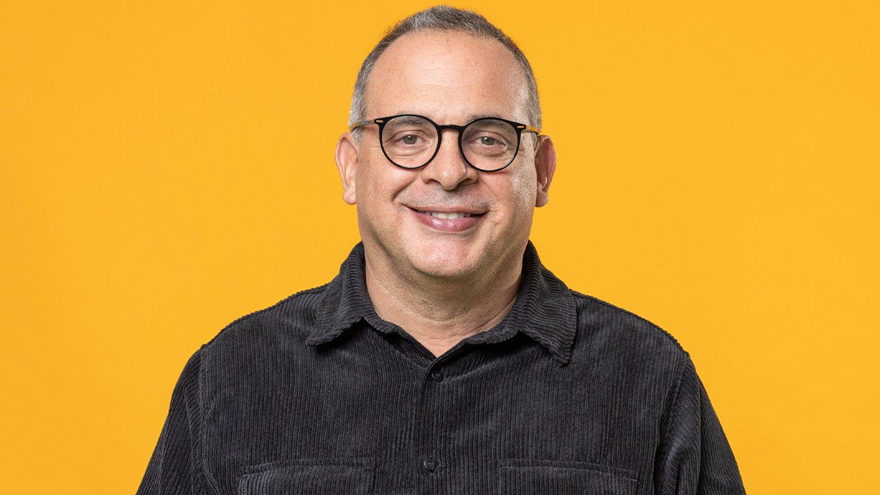 Fabrício Mamberti posando para foto com camisa preta em fundo amarelo