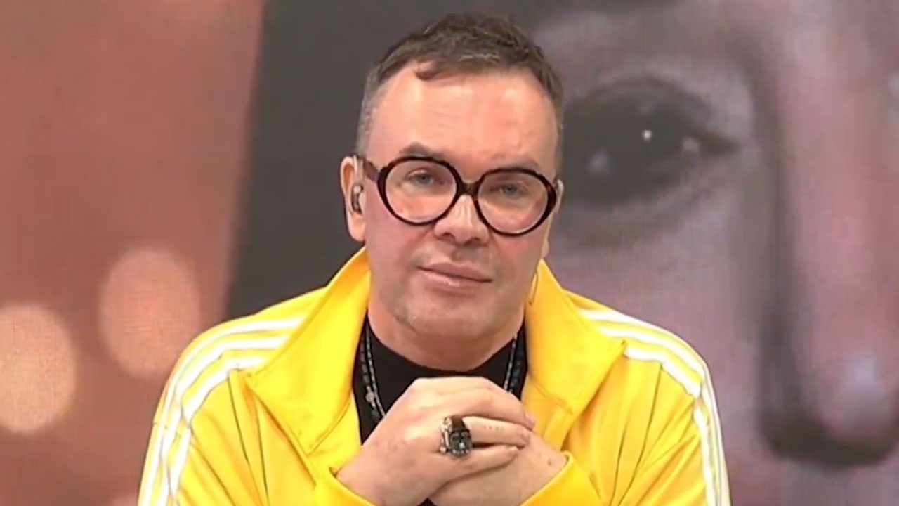 Felipeh Campos de jaqueta amarela em estúdio com imagem de Sonia Abrão desfocada ao fundo