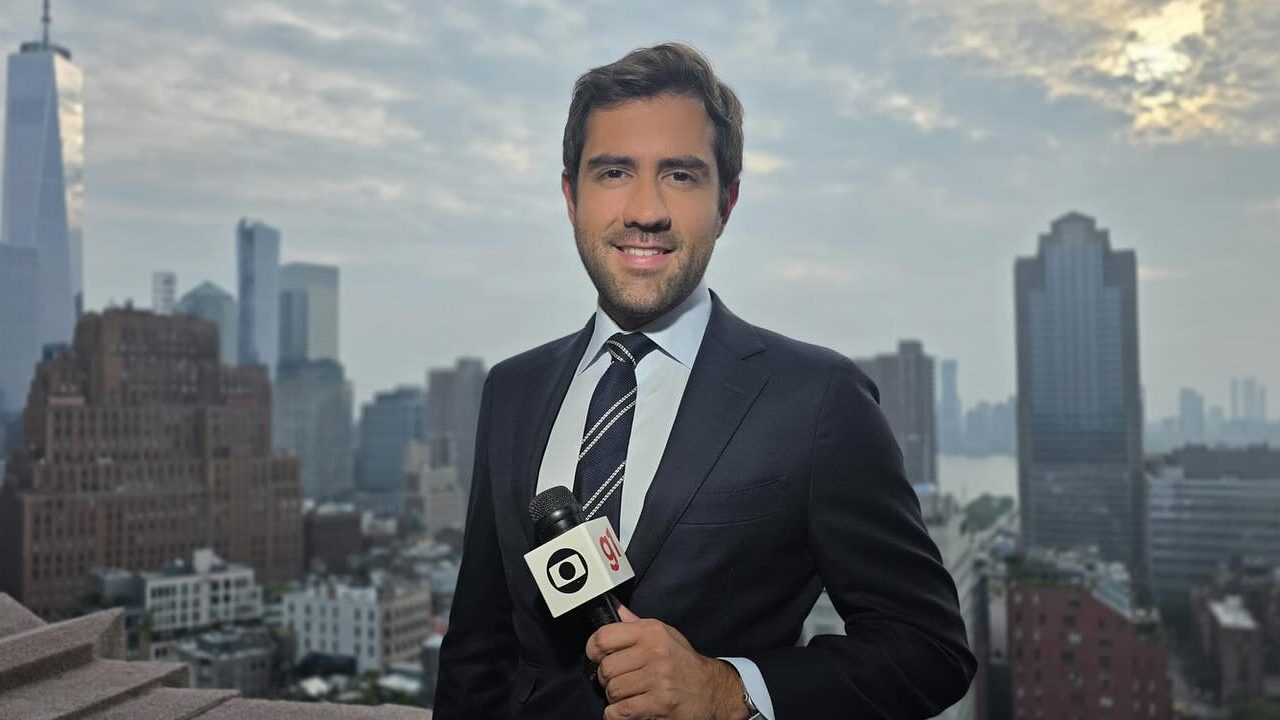 Felippe Coaglio correspondente da Globo em Nova York com microfone em mãos diante de prédios e céu nublado
