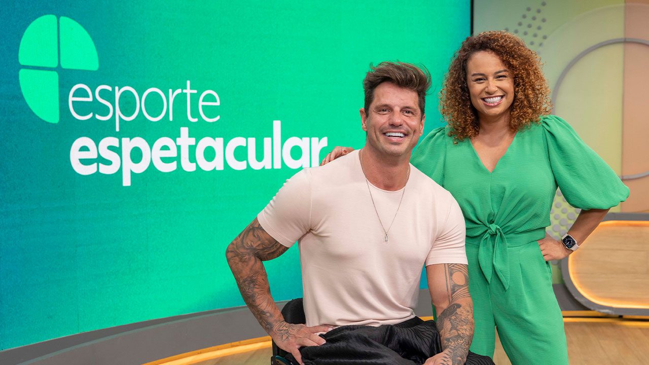 Os apresentadores Fernando Fernandes e Karine Alves posam sorrindo no estúdio do Esporte Espetacular, com o logotipo do programa ao fundo