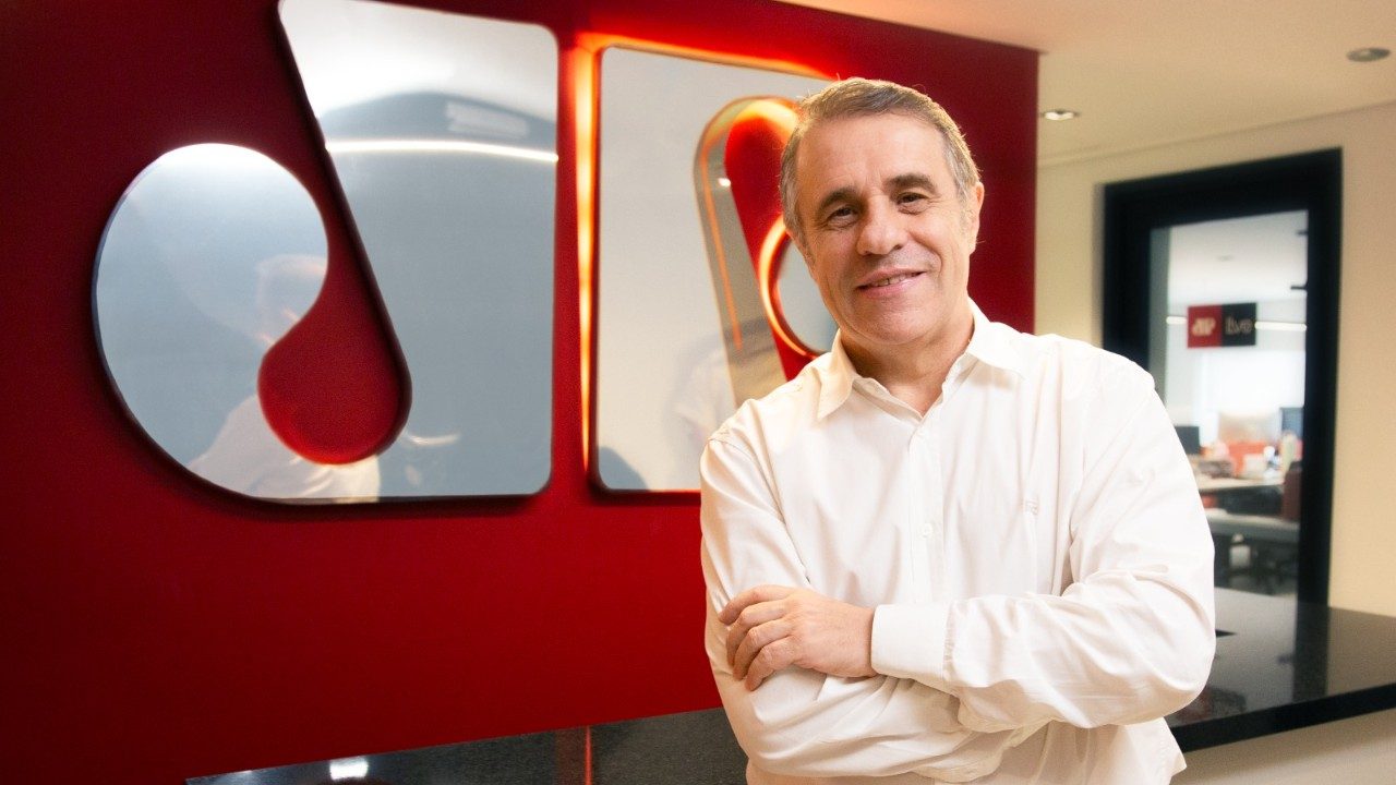 Fernando Pelegio em escritório com parede vermelha e logo da Jovem Pan em destaque ao fundo com iluminação interna