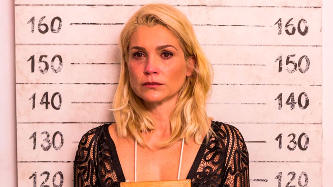 Flávia Alessandra, no elenco de Êta Mundo Melhor!, caracterizada como Sandra em cena de prisão com expressão chorosa diante de parede de altura policial