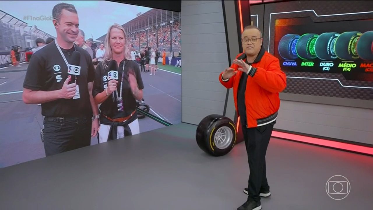 Apresentador de TV em estúdio fala sobre automobilismo enquanto gesticula ao lado de um pneu de Fórmula 1. Em um grande telão atrás dele, dois repórteres aparecem em um autódromo lotado, e outro painel mostra os diferentes tipos de pneus usados nas corridas. No canto da tela aparece o logotipo da TV Globo.