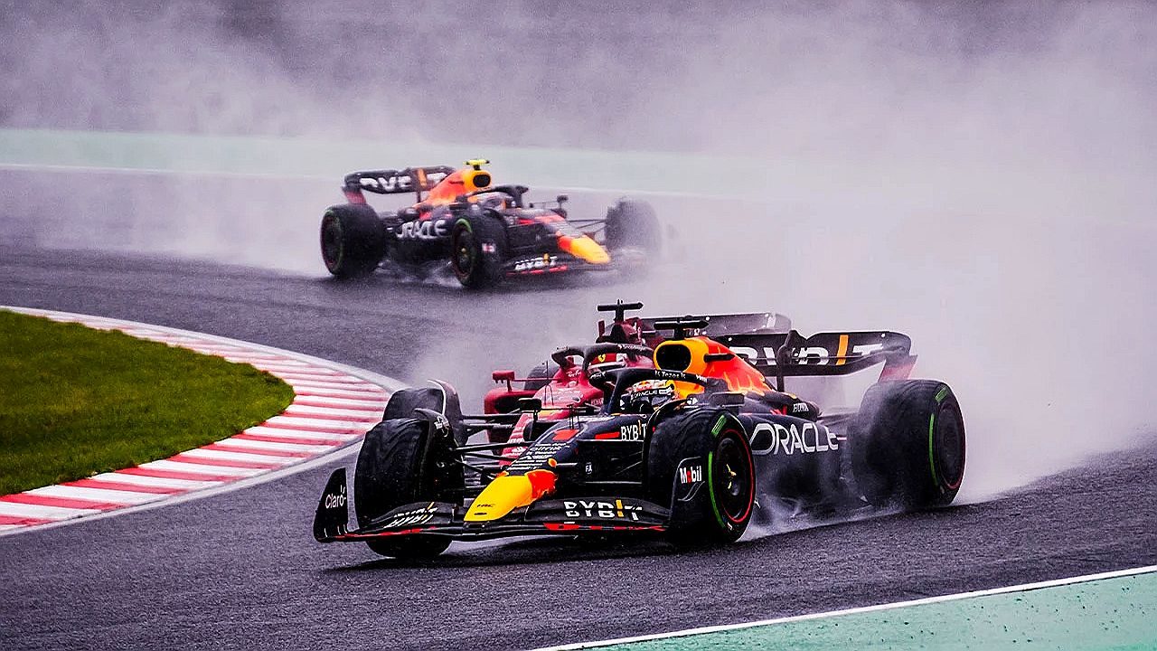 Carros da Fórmula 1 disputam curva sob chuva com spray de água em corrida automobilística