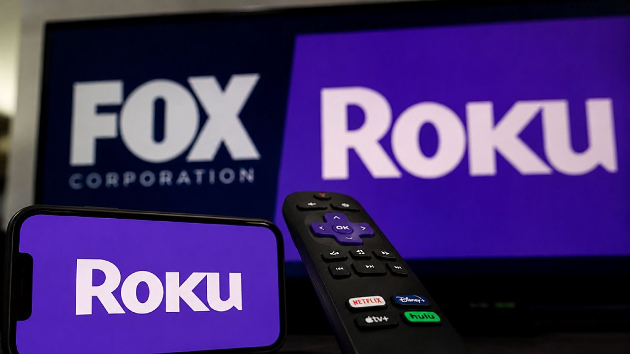 Logotipos da Roku e da Fox exibidos em tela de TV com controle remoto e smartphone em destaque