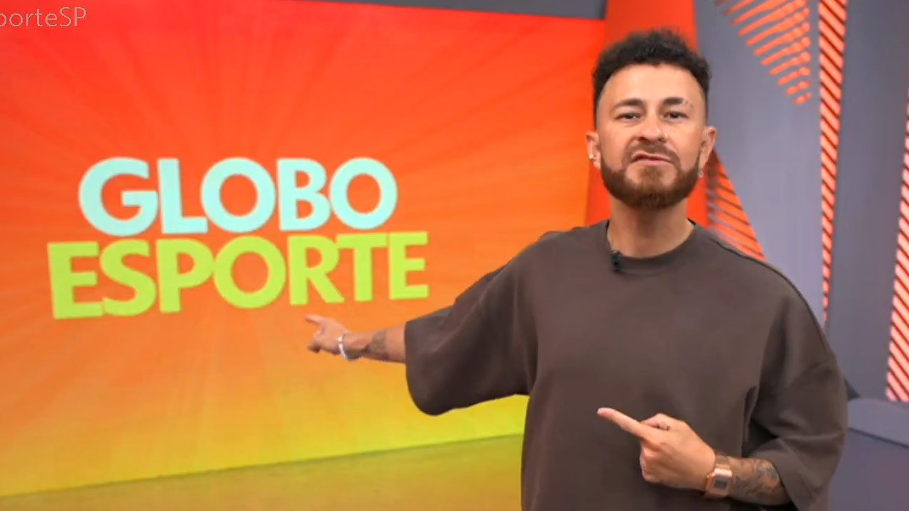 Fred Bruno apresenta o Globo Esporte SP apontando para o telão com o logotipo do programa no estúdio da Globo