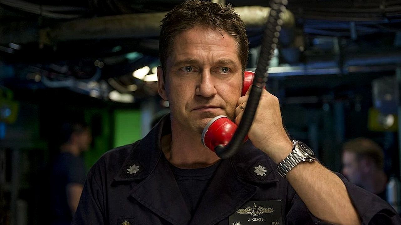 Militar segura telefone vermelho em ambiente de comando enquanto fala com expressão séria