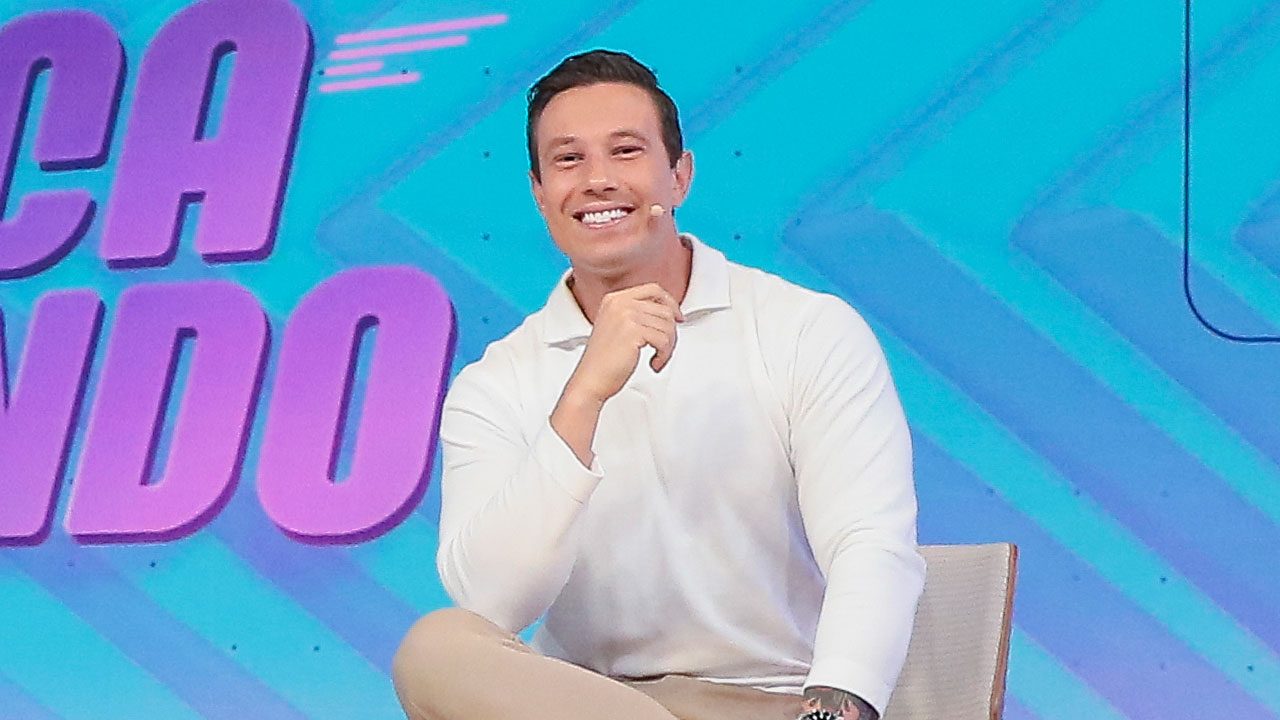 Gabriel Cartolano sorrindo sentado no estúdio do Fofocalizando com microfone no rosto