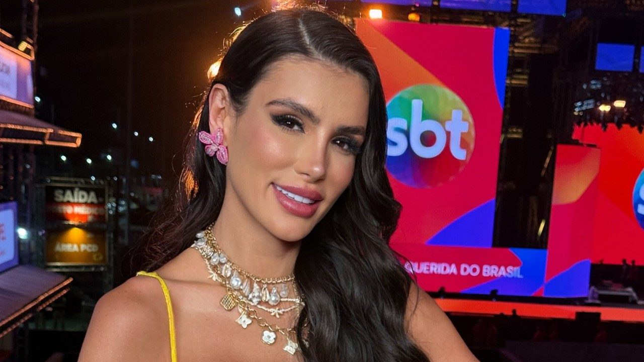 Gaby Cabrini posa com vestido amarelo e joias diante de painel do SBT em evento de música
