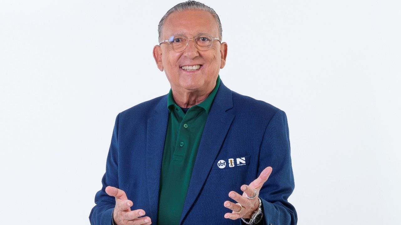 Galvão Bueno posa sorrindo com blazer azul e camisa verde em foto promocional do SBT