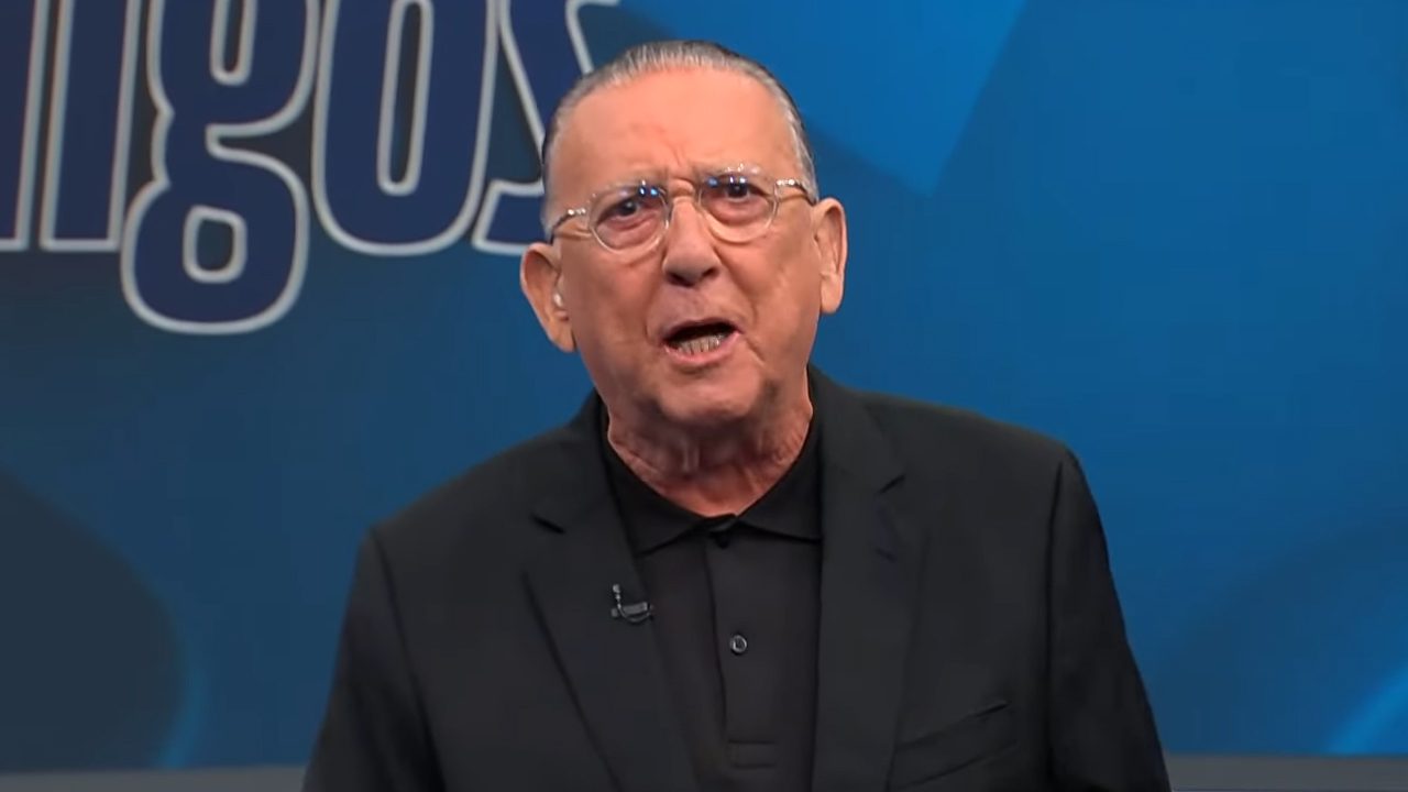 Galvão Bueno de óculos e blazer preto falando no estúdio de programa esportivo da Band com fundo azul