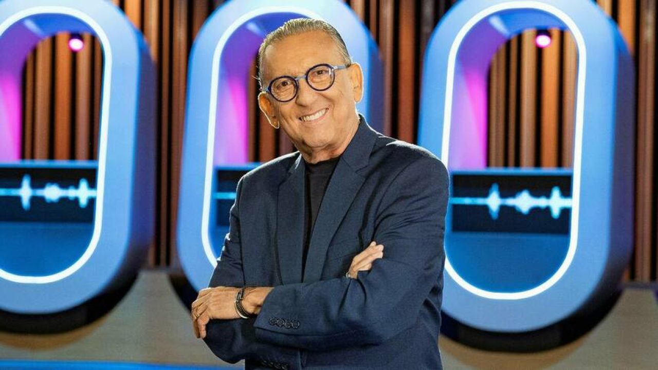 Galvão Bueno sorrindo com os braços cruzados em estúdio de TV