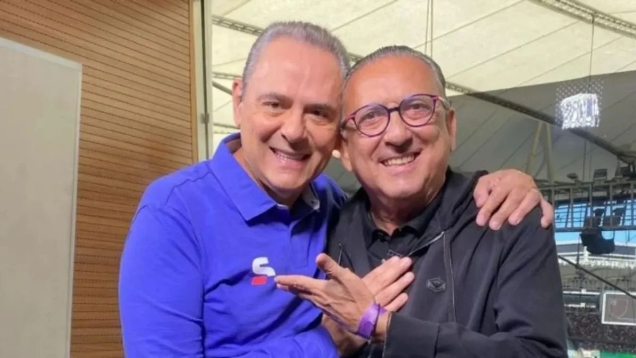 Dois homens sorrindo abraçados em camarote de estádio durante evento esportivo